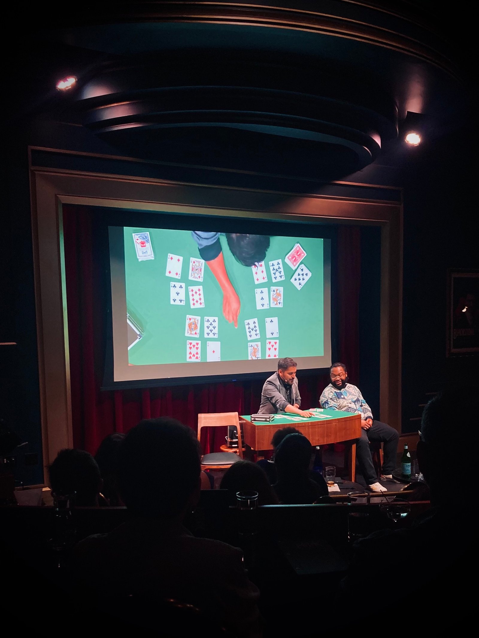 Alejandro performing card magic with an audience volunteer in a theater